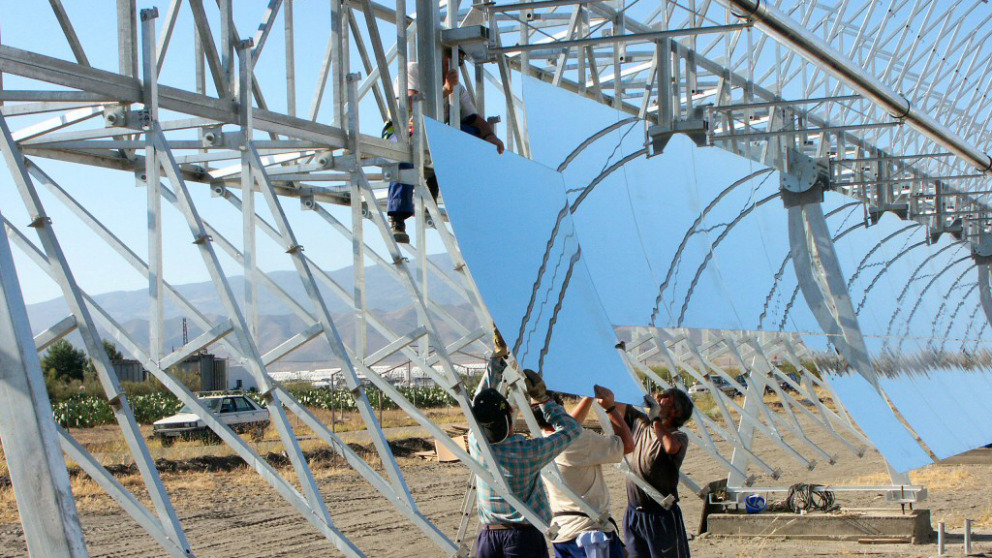 In einem solarthermischen Kraftwerk in Spanien montieren Arbeiter Spiegel an einen Parabolrinnenkollektor.